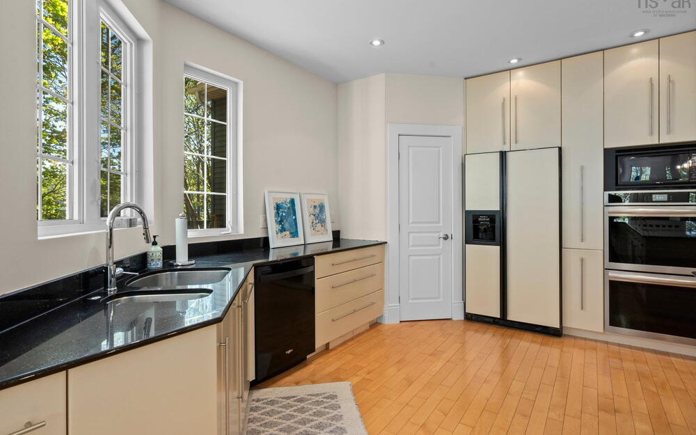 Kitchen with black appliances, a sink, dark stone countertops, cream cabinetry, and light wood-type flooring