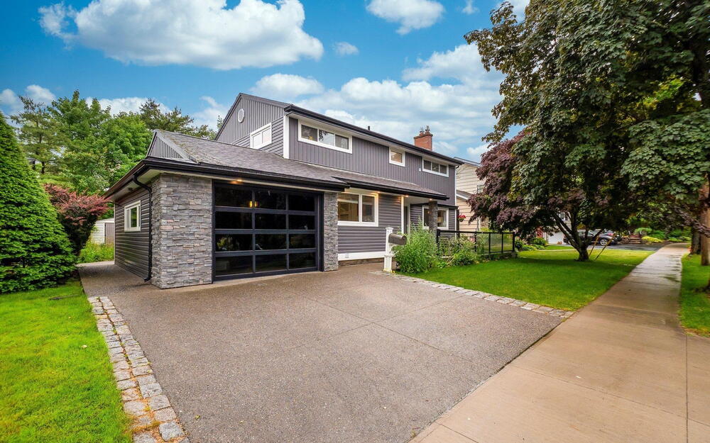 View of front facade featuring stone siding, a front yard, a chimney, driveway, and board and batten siding