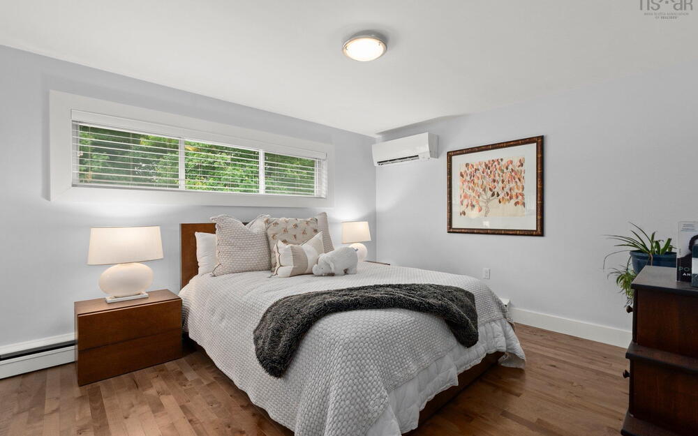 Bedroom with a wall mounted AC, a baseboard radiator, and wood finished floors