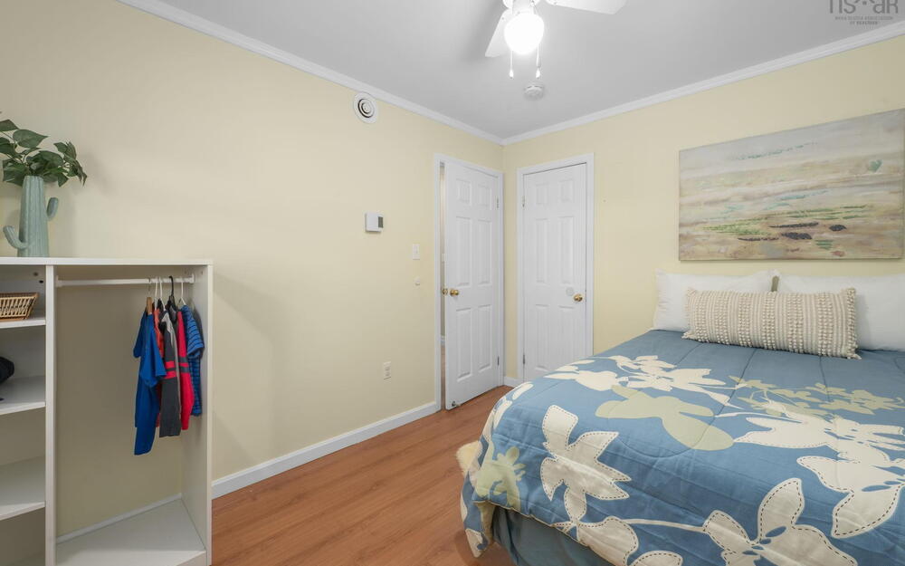 Bedroom featuring wood-finish flooring, two white panel doors, a ceiling fan with integrated lighting, and crown molding