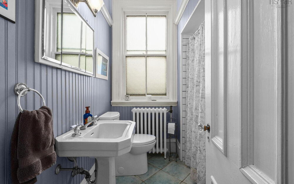 Bathroom featuring beadboard wall paneling, a white porcelain pedestal sink, a classic cast-iron radiator, a double-hung window, and tile flooring