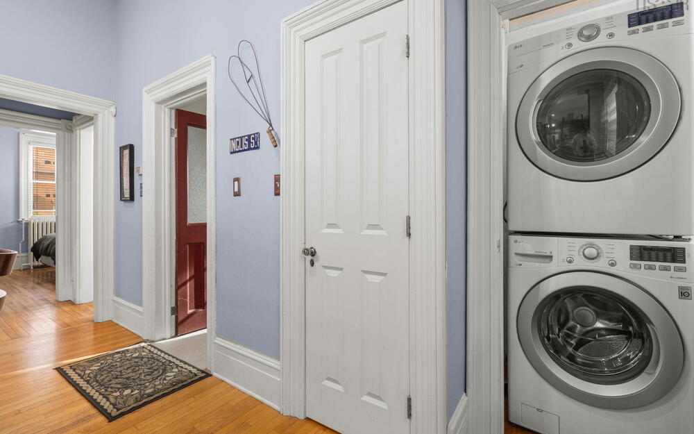 Stacked front-loading laundry unit, original wood-finish flooring, and classic interior millwork featuring detailed door casing and trim