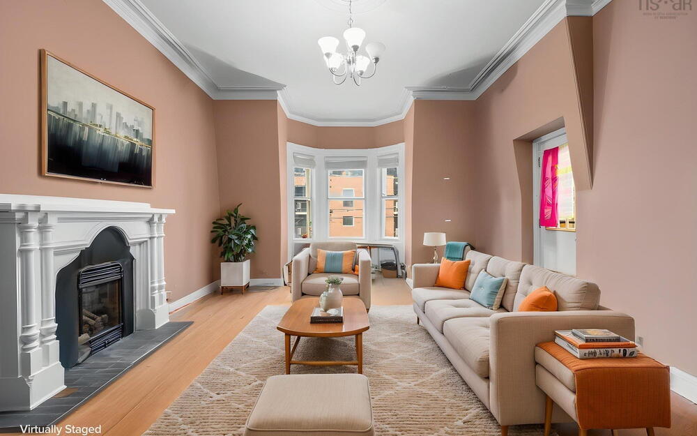 Living area featuring a fireplace with an ornate mantel, bay windows, wood-finish flooring, ceiling medallion, and crown molding