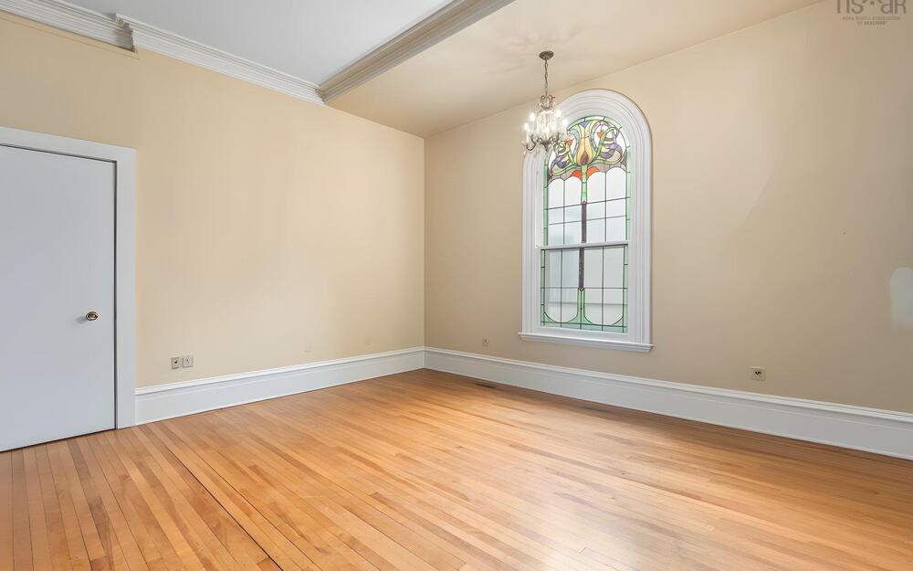 Arched stained-glass window, wood-finish flooring, crown molding, and multi-light chandelier