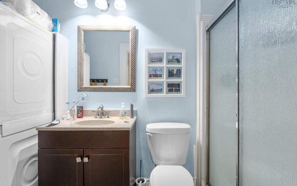 Bathroom featuring a vanity with a stone-finish countertop, integrated sink, and polished metal faucet, complemented by a tri-light fixture, framed wall mirror, and walk-in shower with a sliding glass enclosure