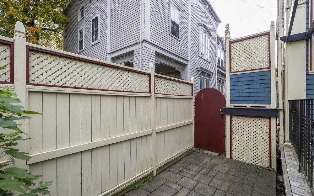 Paver stone patio area enclosed by a solid vinyl privacy fence with decorative lattice detailing and a solid wood gate