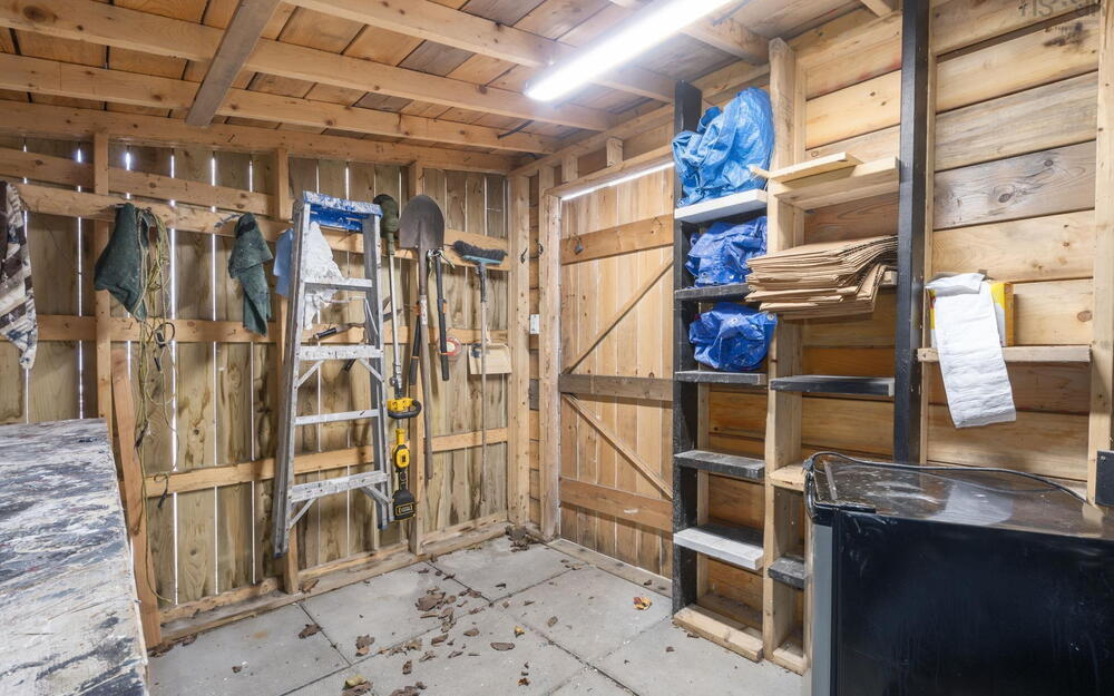 Storage structure featuring exposed wood-plank walls and ceiling, concrete flooring, built-in wooden shelving, and an integrated overhead lighting fixture