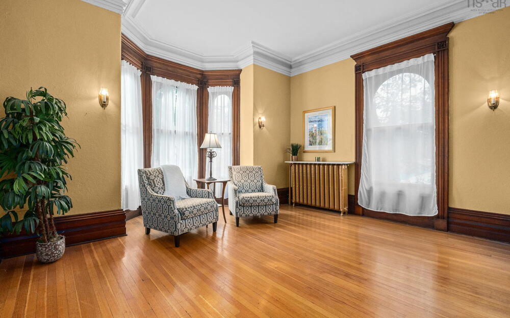 Hardwood flooring, bay window with arched detailing, ornate wood trim and casing, crown molding, and metal radiator