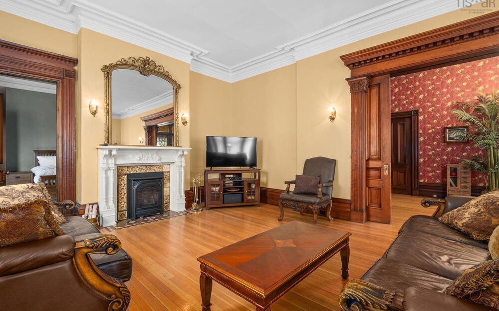 Hardwood flooring, elaborate crown molding, stained wood door casings, and a fireplace with a decorative mantel and tile hearth